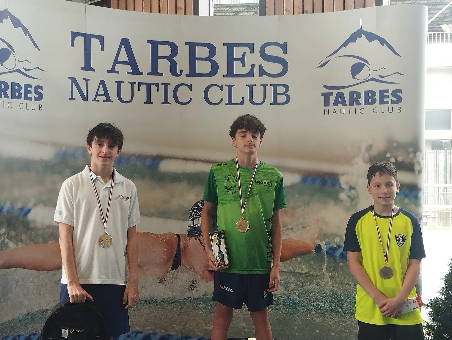 Trois nageurs lourdais médaillés devant la bâche du Tarbes Nautic Club