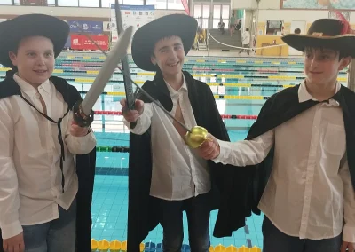 Trois nageurs du club déguisés en mousquetaires au bord du bassin lors des Médailles du TOAC